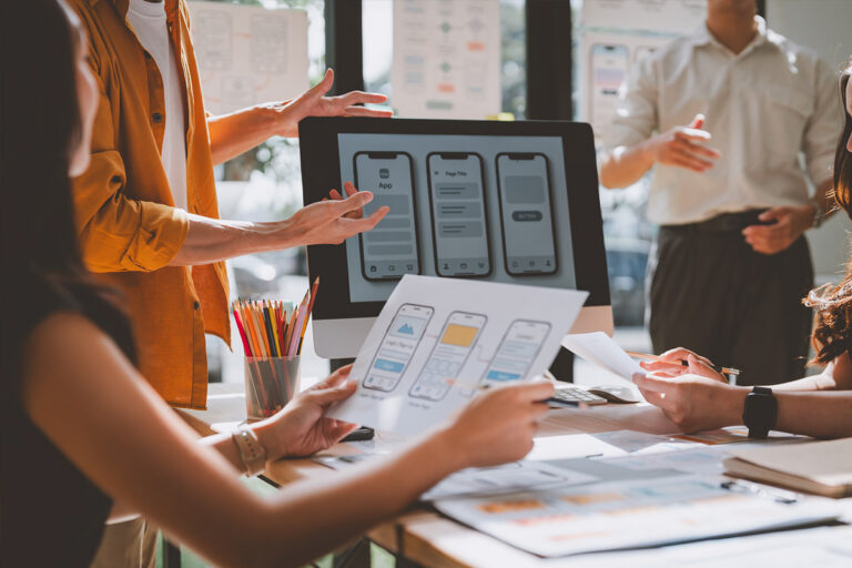UI/UX design team presenting and reviewing mobile app wireframes during a collaborative product planning meeting in a modern office.