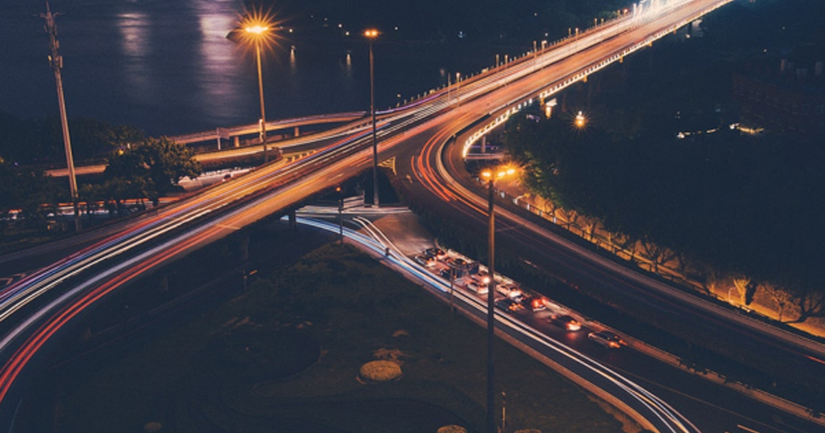 Aerial night view of highway interchanges with light trails.