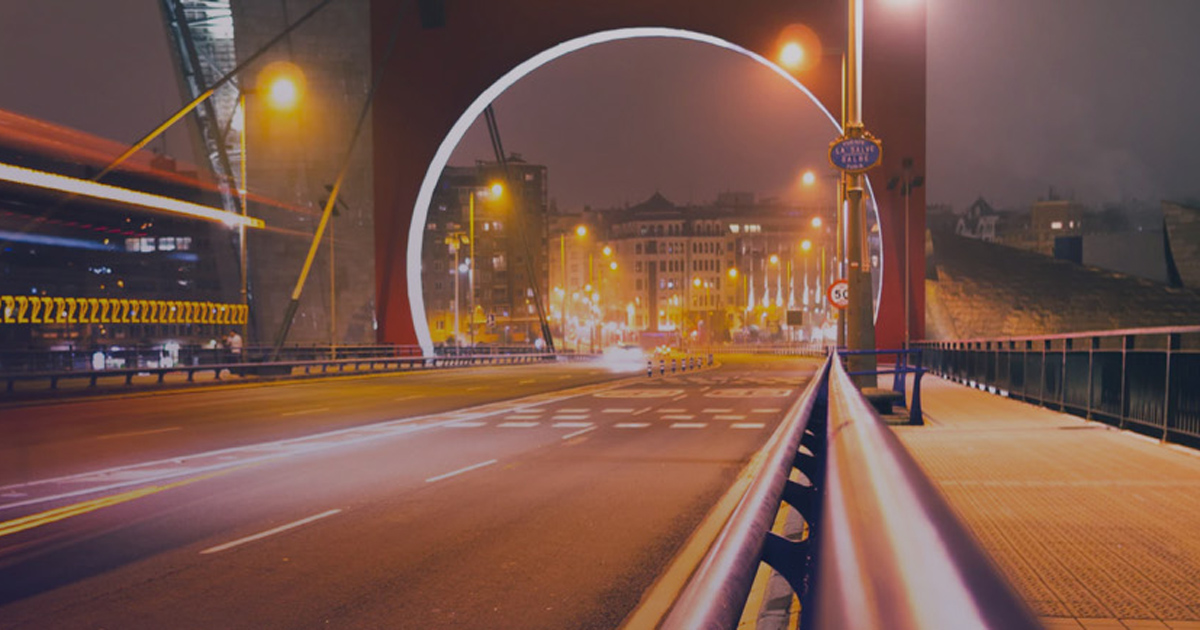 Long-exposure night highway leading to an illuminated arch bridge.