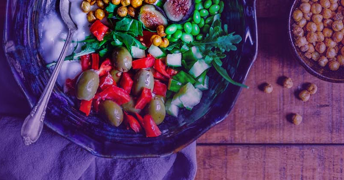 Bowl of fresh salad with olives, peppers, and greens beside roasted chickpeas.