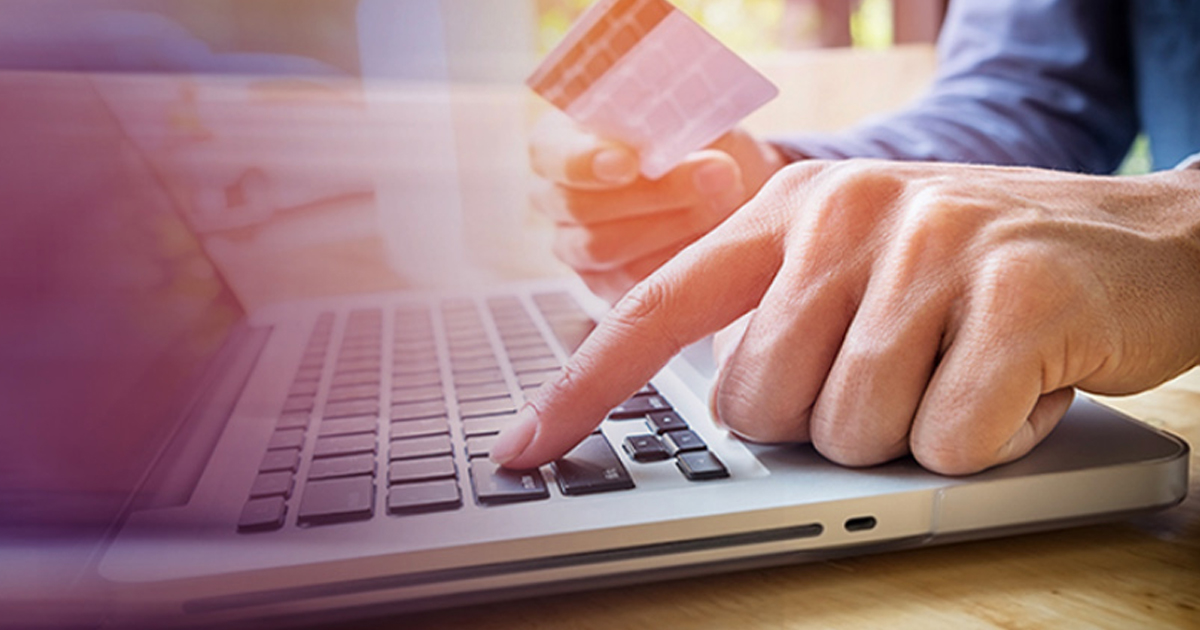 Hand holding a credit card while typing on a laptop, representing merchants protecting online payments during the COVID-19 crisis.