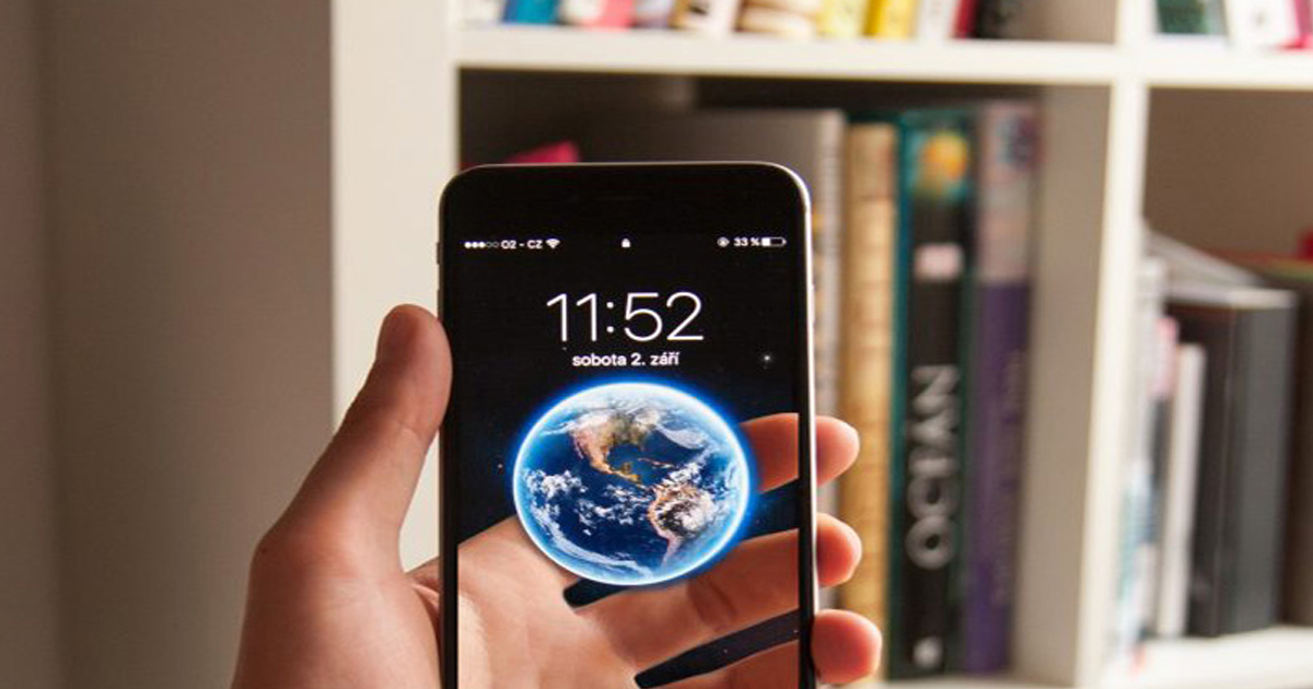 Hand holding a smartphone with a small globe hovering over it in front of a bookshelf, representing the internet's future importance.