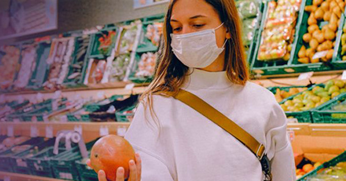 Shopper wearing a face mask holding fruit in a grocery store aisle, representing the food service industry during COVID-19.