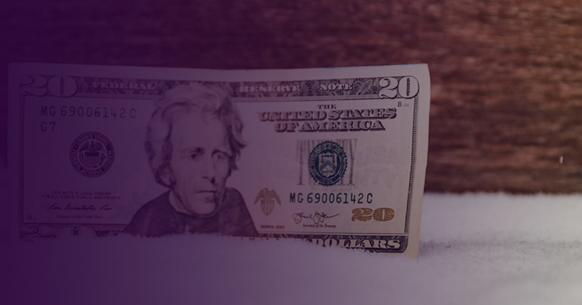 Twenty-dollar bill resting on a snowy surface in purple light, representing the finance industry frozen during COVID-19.