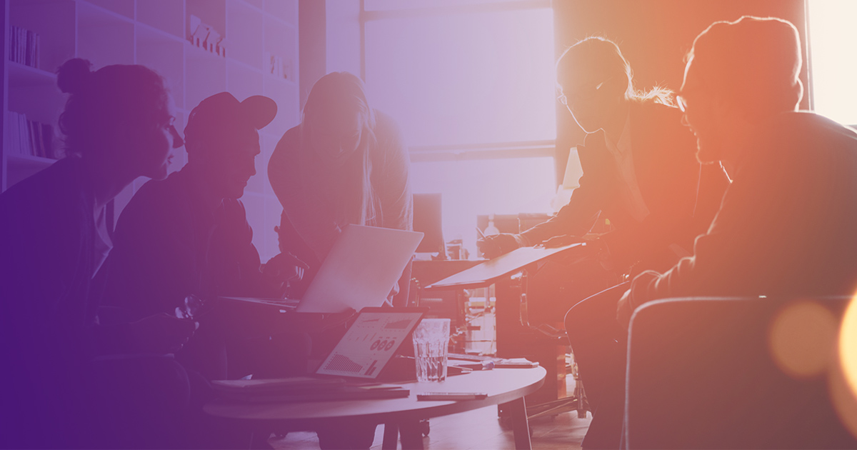 Team meeting around a table silhouetted against a bright window.