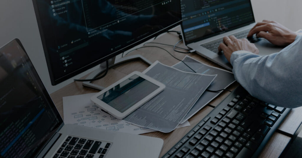Developer working at a desk with code on a monitor and laptop.