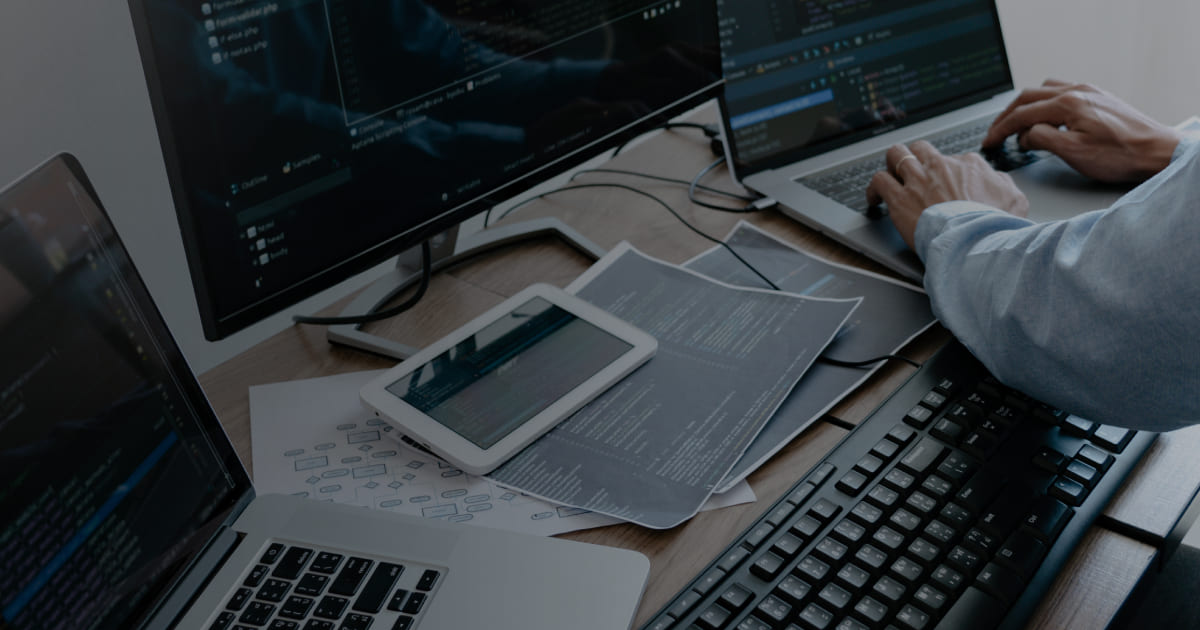 Developer working at a desk with code on a monitor and laptop.