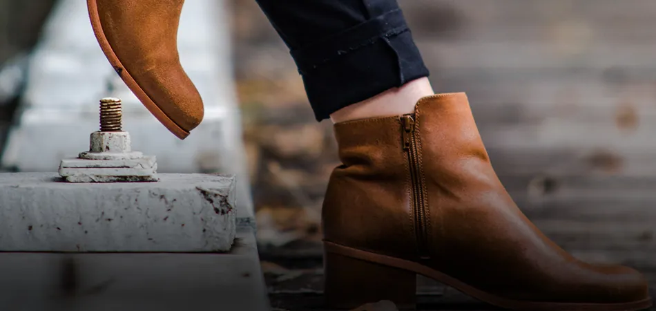 Person wearing brown ankle boots stepping beside a concrete structure